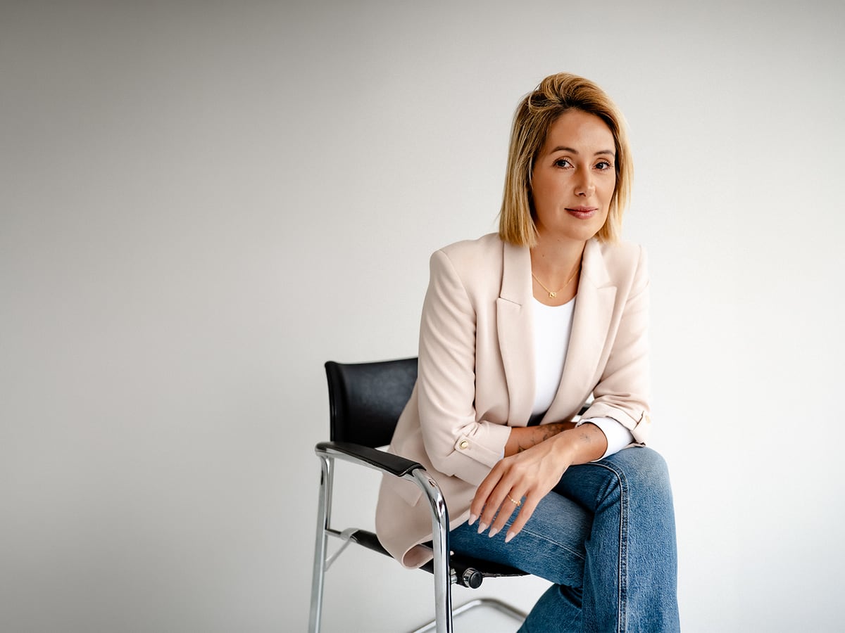 Carolina Vogels sentada em seu escritório, de blazer e jeans
